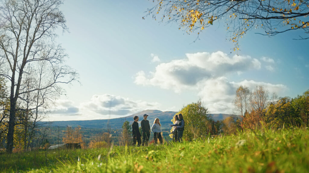 Personer står på en äng med fjäll i bakgrunden