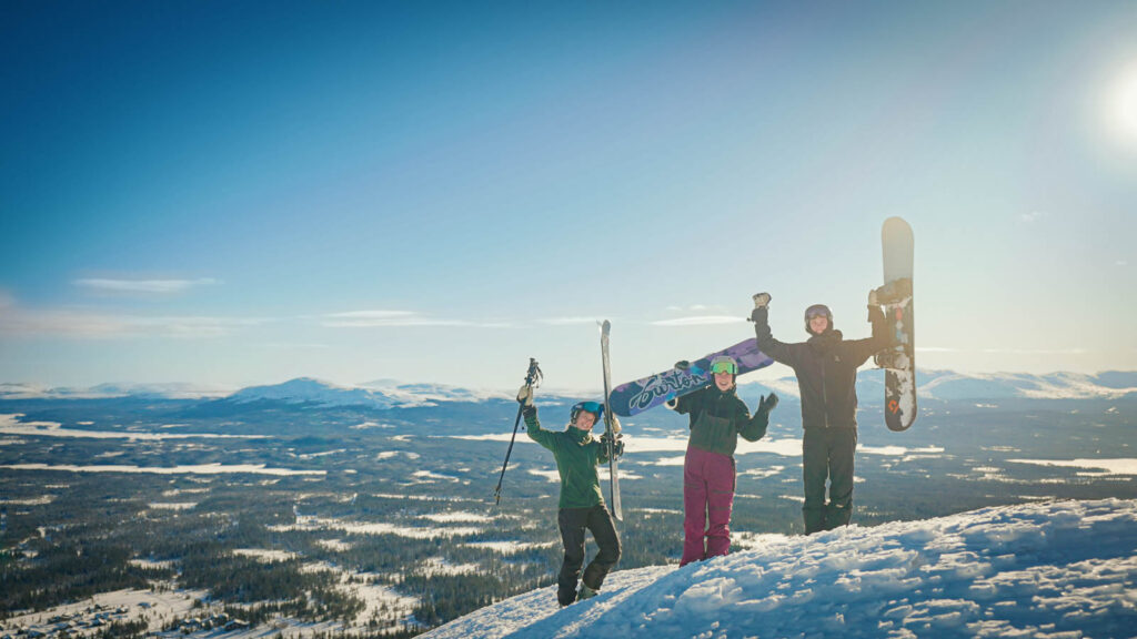 tre glada snowboardåkare som står på en bergstopp i motljus